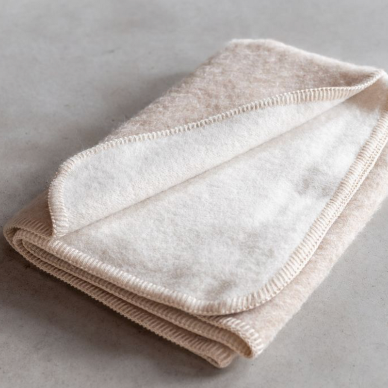 Plaid laine bebe beige plié posé sur un sol couleur neutre