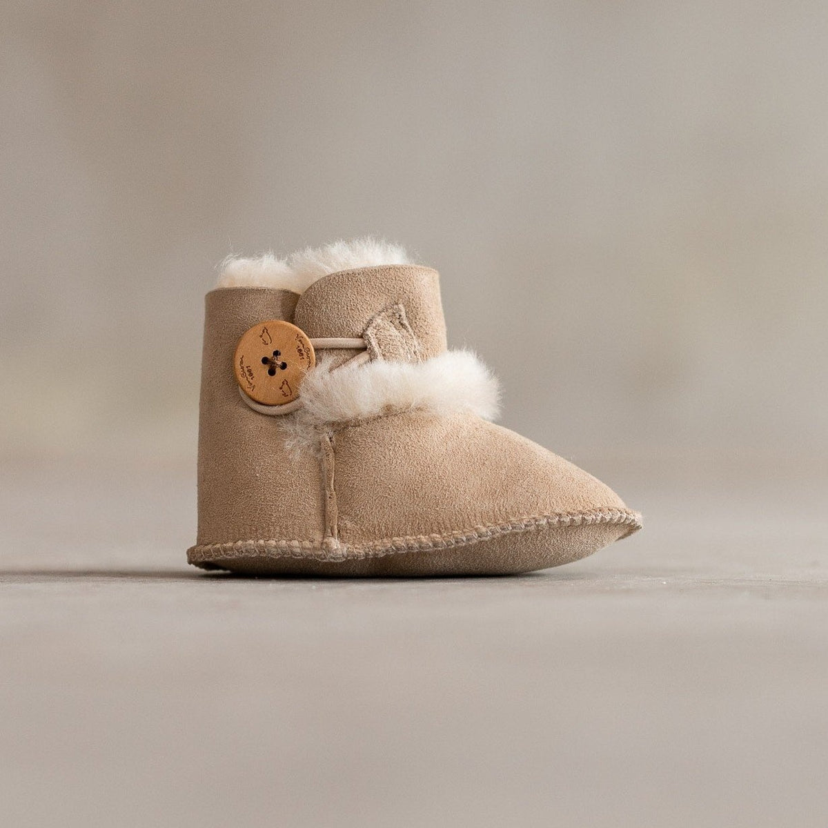 Chaussons bébé en peau d'agneau blanc, vu de profil, bouton en bois et revers en laine