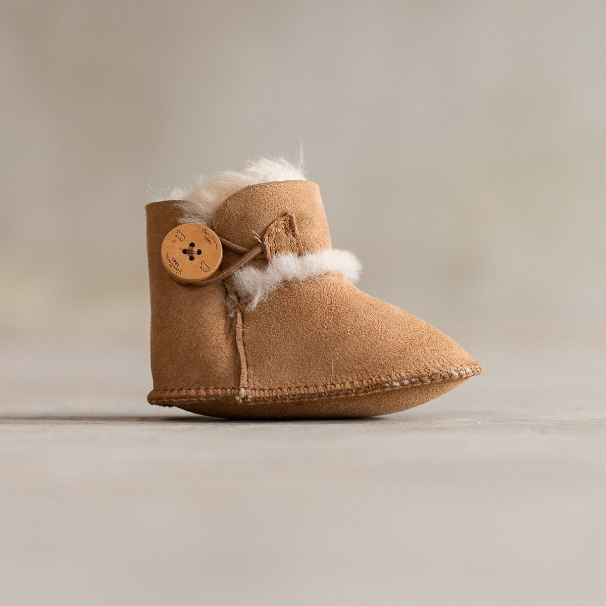 Chaussons bébé en peau d'agneau camel, vu de profil, bouton en bois et revers en laine