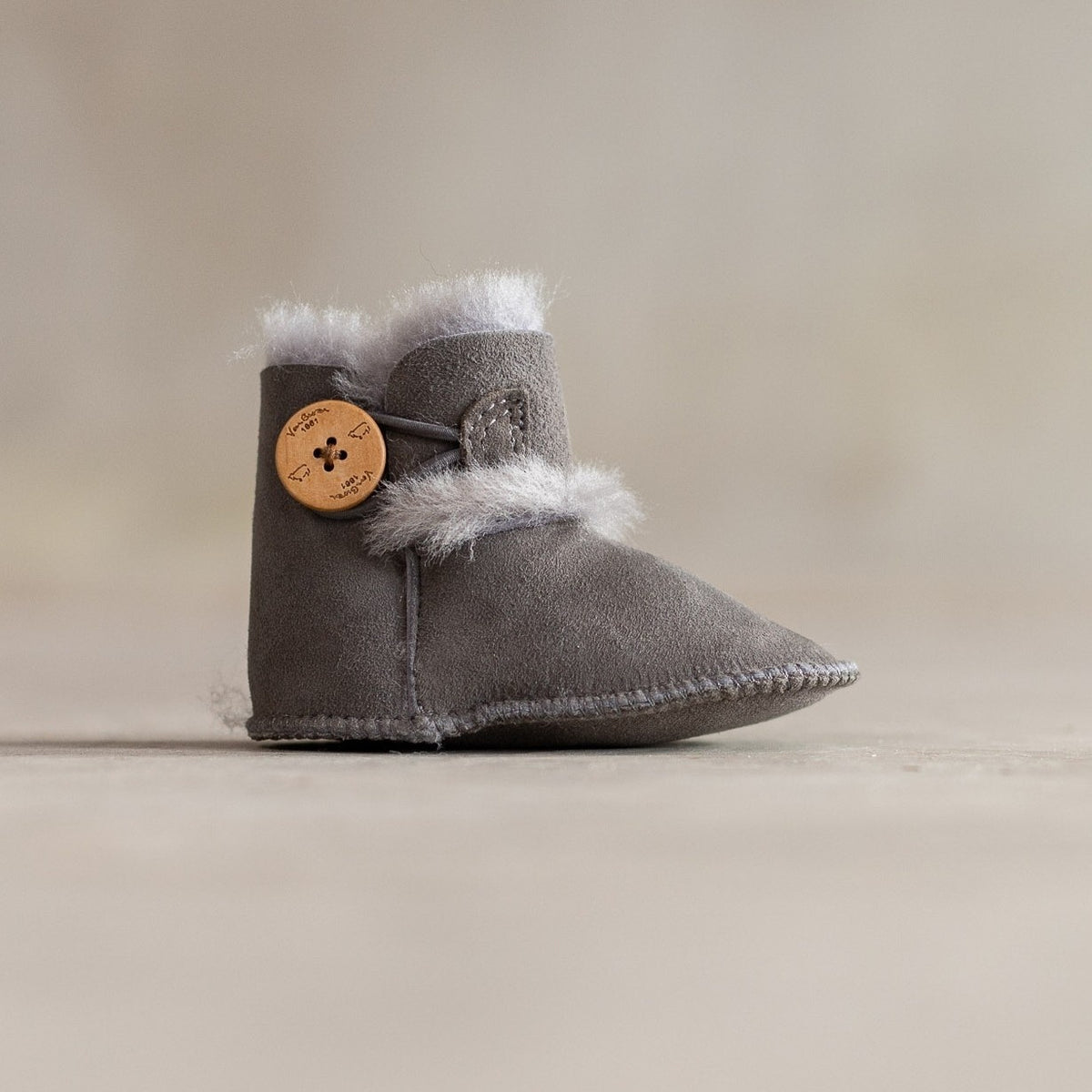 Chaussons bébé en peau d'agneau gris, vu de profil, bouton en bois et laine blanche au revers