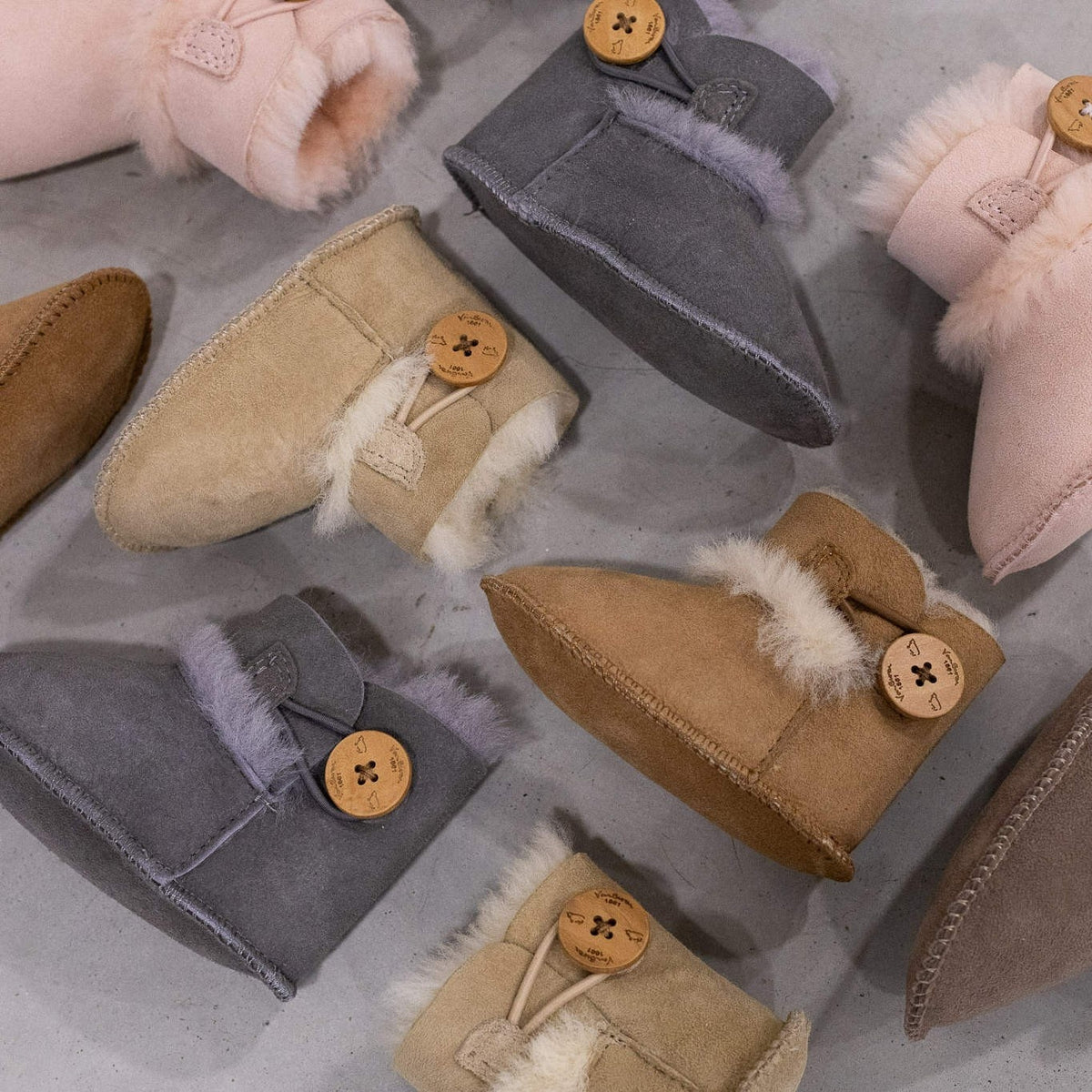 Chaussons bébé en peau d'agneau gris, chaussons de plusieurs couleurs posés à plat