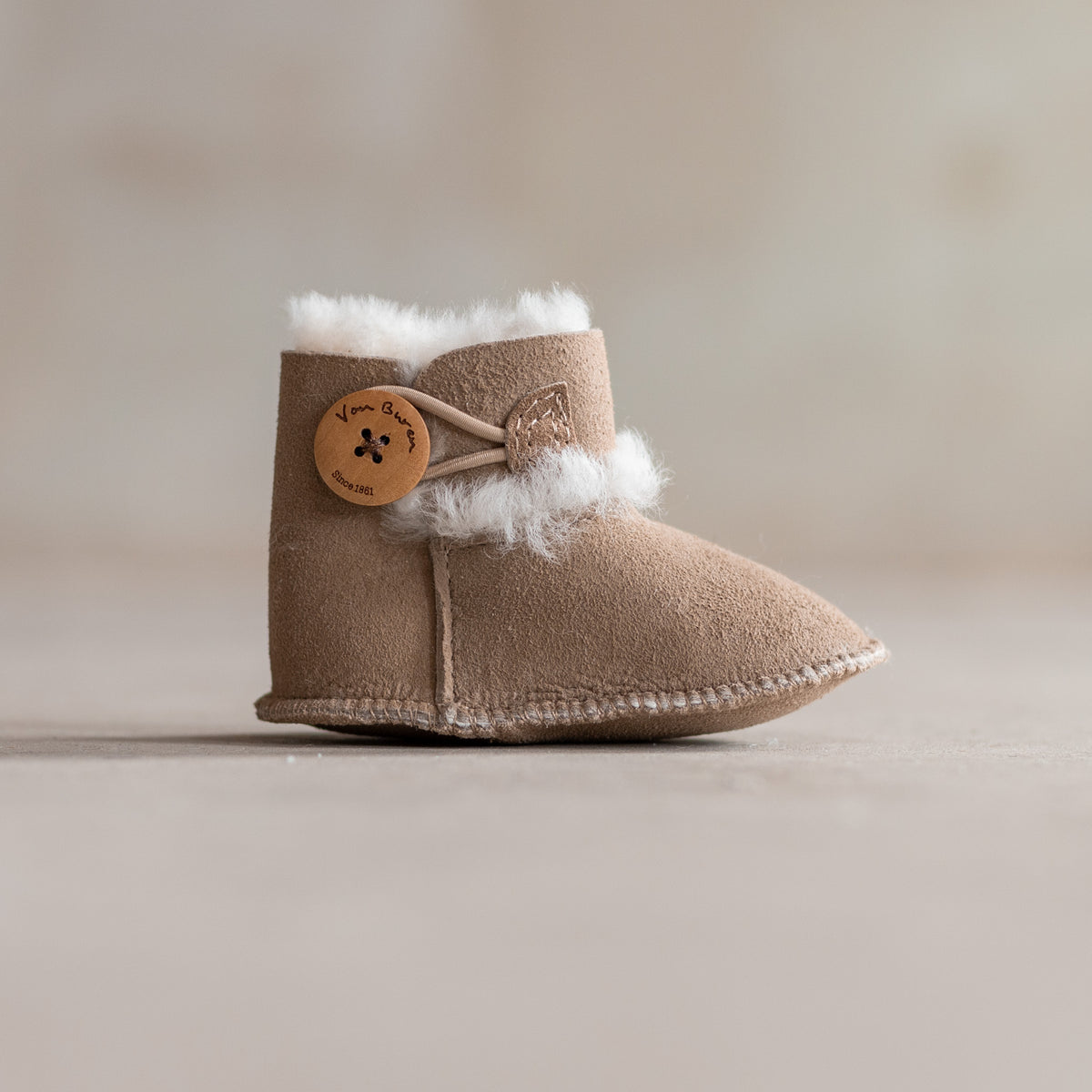 Chaussons bébé en peau d'agneau taupe, vu de profil, bouton en bois et laine qui dépasse du revers