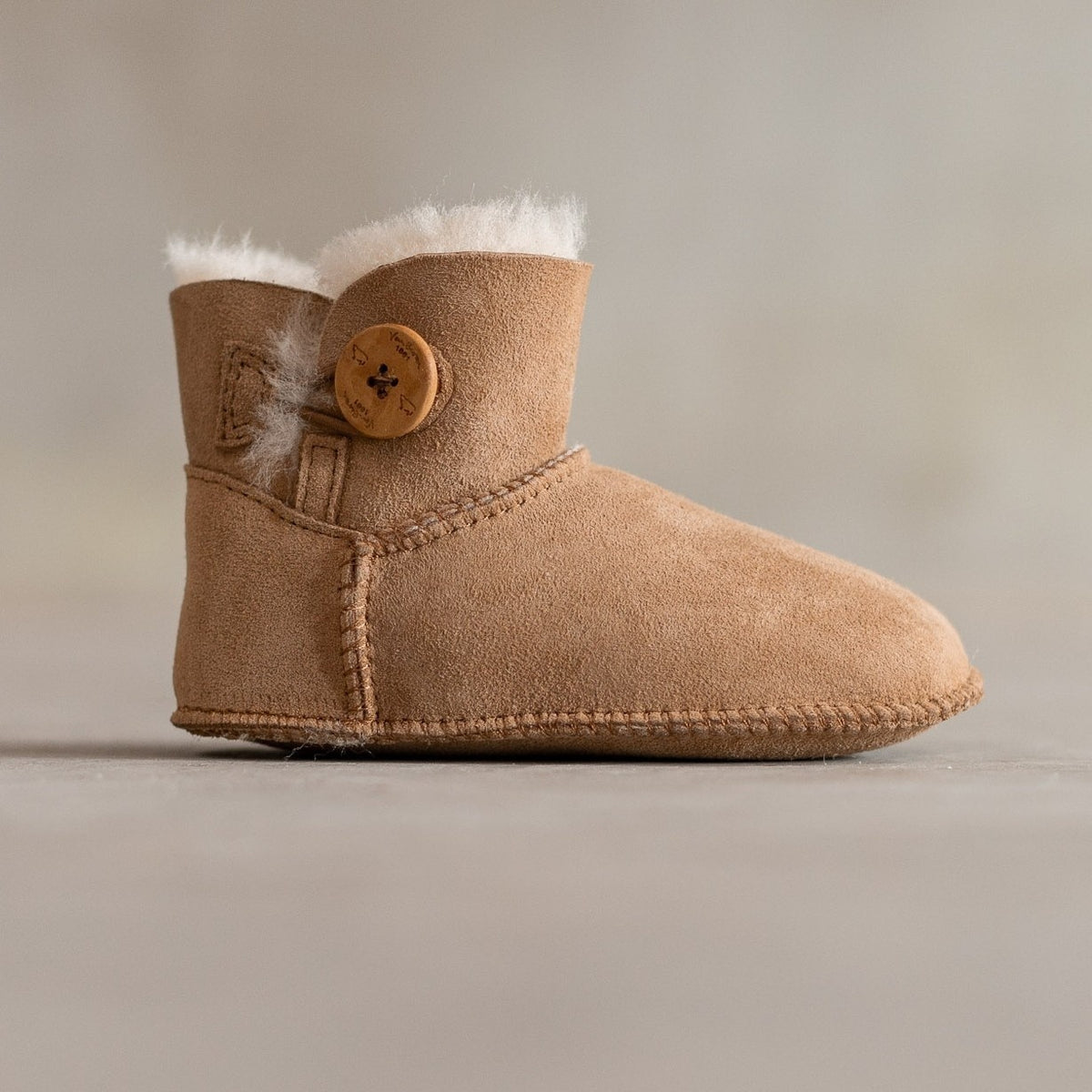 Chaussons enfant en peau d'agneau camel, vu de profil, bouton en bois et revers en laine