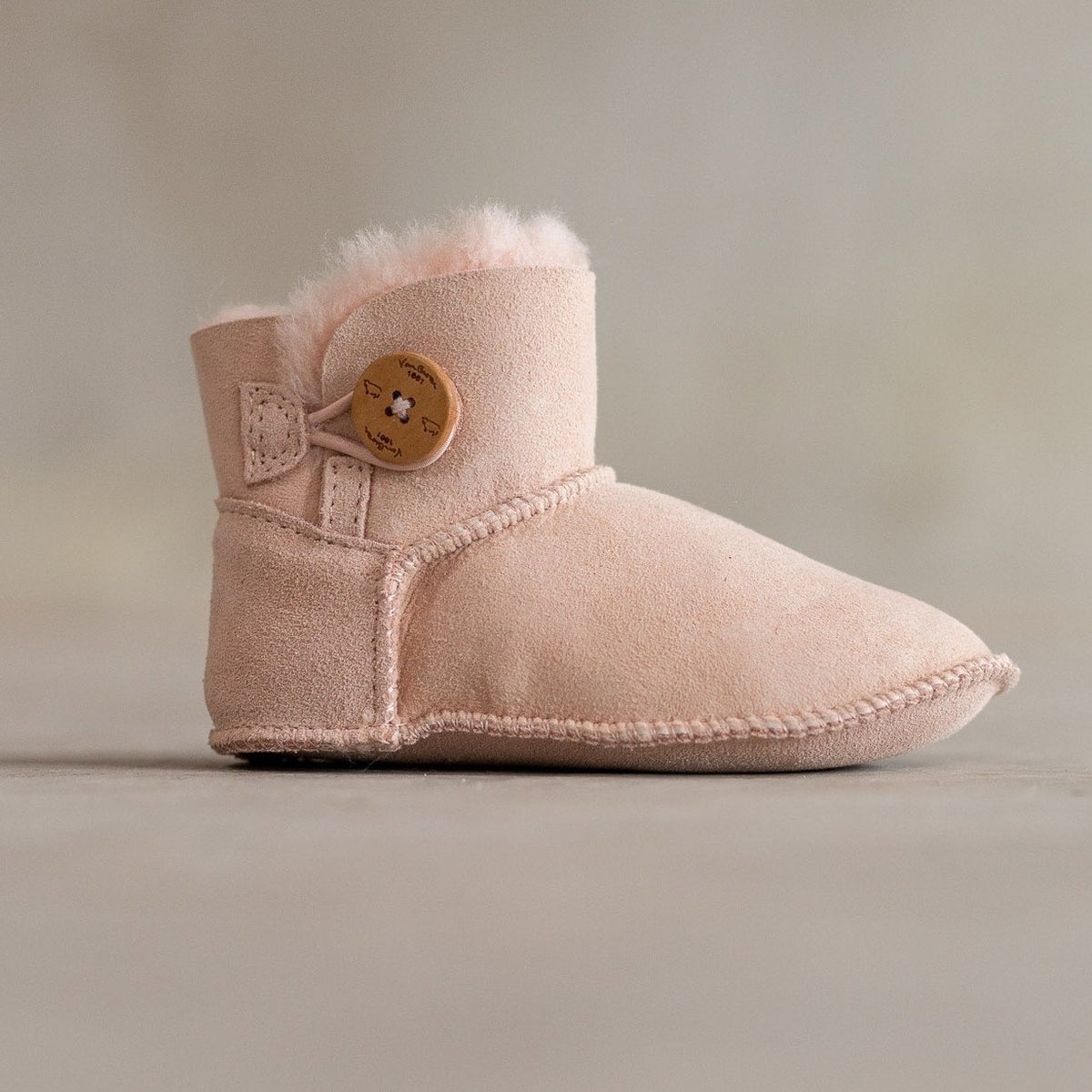 Chaussons enfant en peau d'agneau rose, vu de profil, bouton en bois et revers en laine