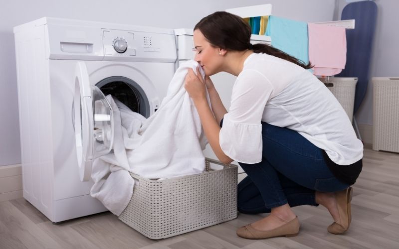 Femme accroupi devant sa machine à laver, sortant du linge blanc et le sentant.