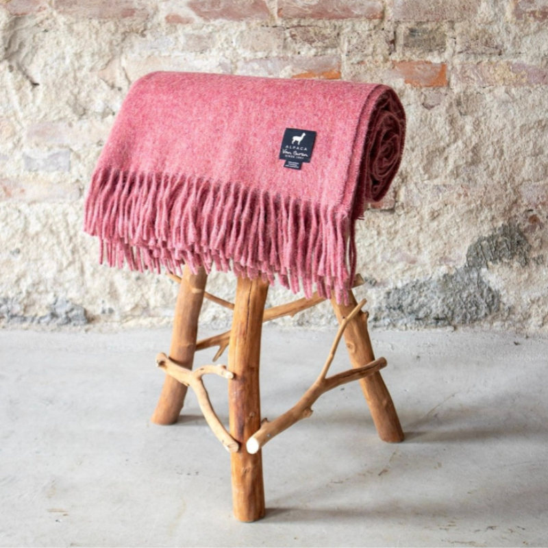 Plaid laine chaud rose posé sur un tabouret en bois