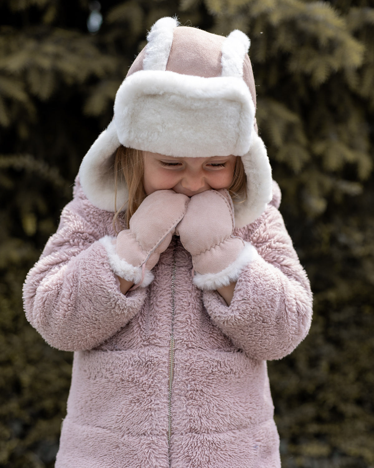 Bonnet aviateur bébé et enfant en peau de mouton rose, porté par une petite fille qui rit