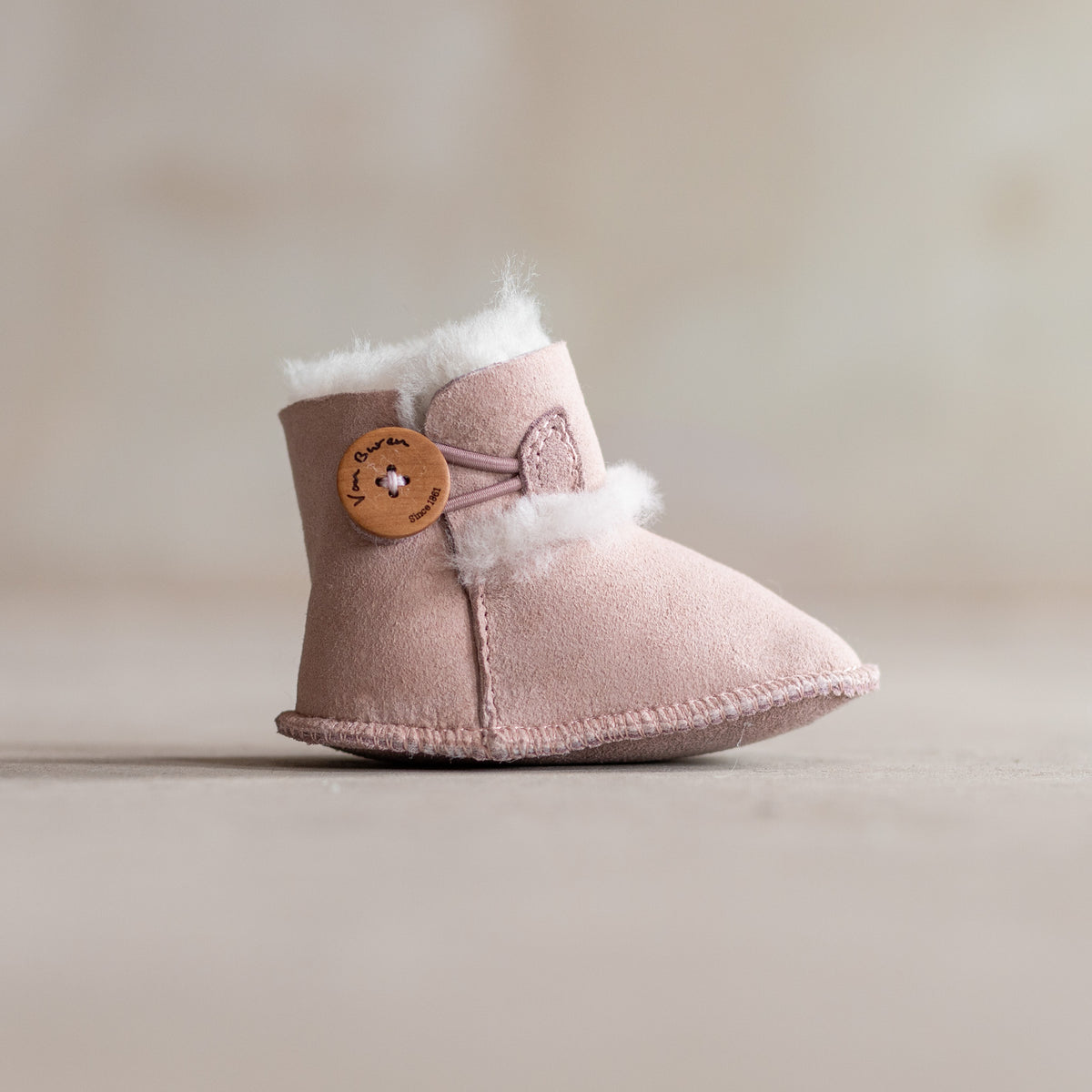 Chaussons bébé en peau d'agneau rose, vu de profil, bouton en bois et revers en laine