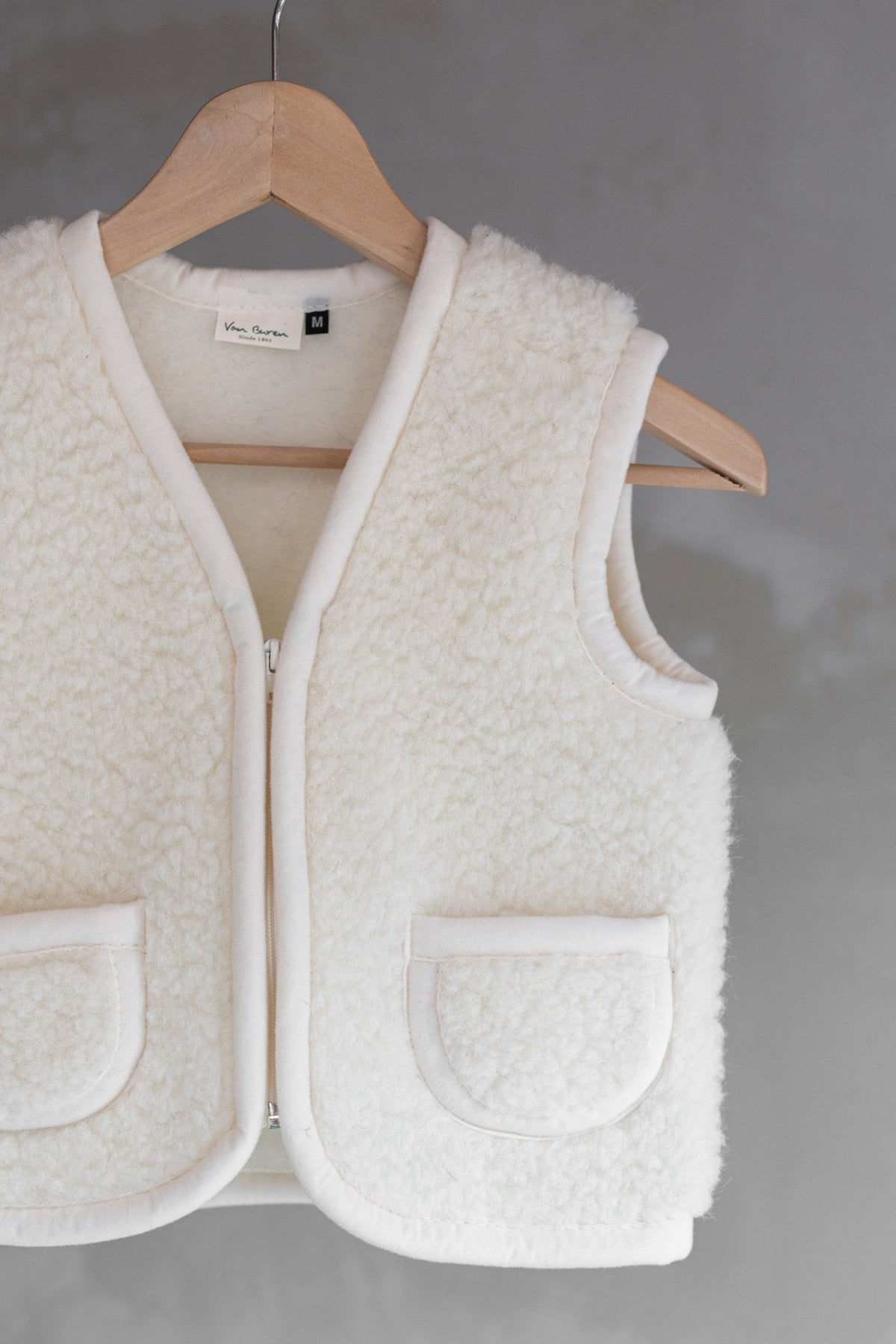 Gilet sans manches en laine pour enfant blanc cassé, suspendu à un cintre