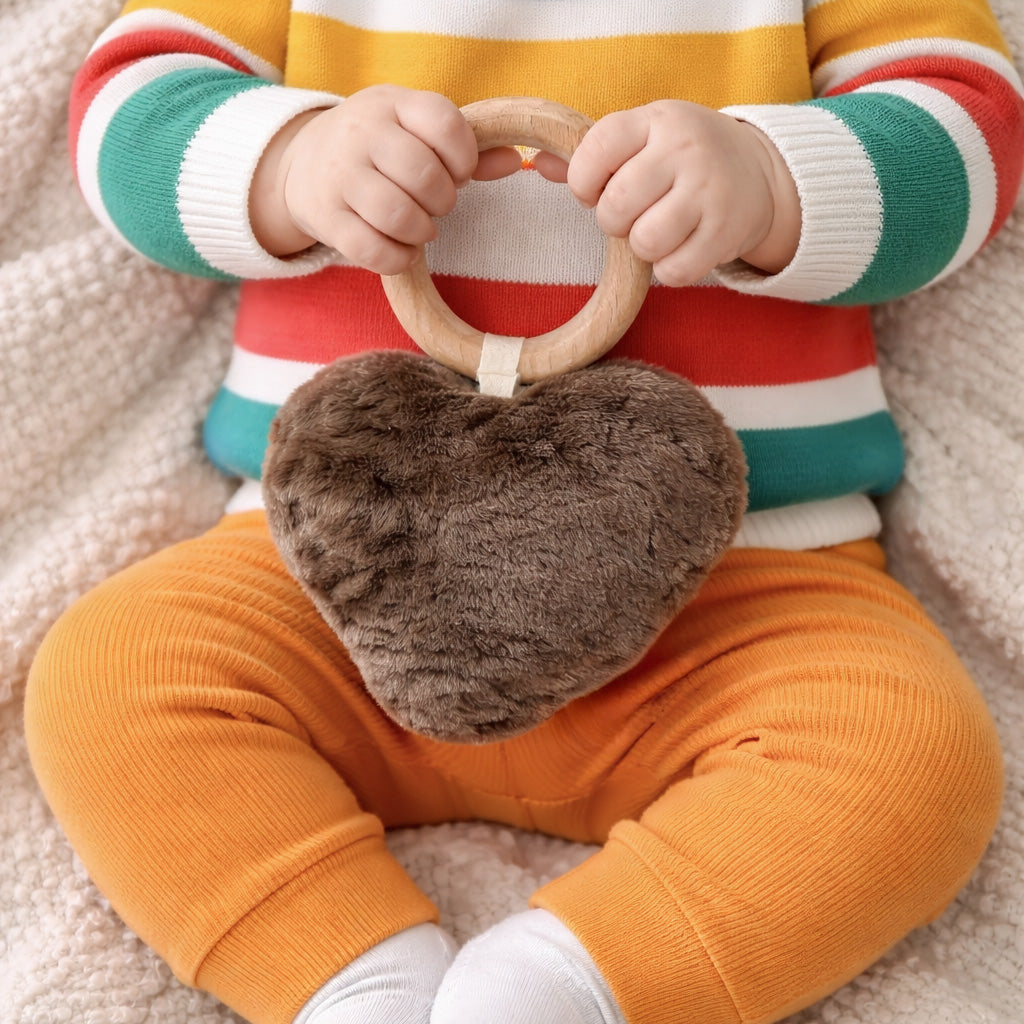 Hochet cœur en peau d'agneau taupe, tenu par un bébé en pull rayé