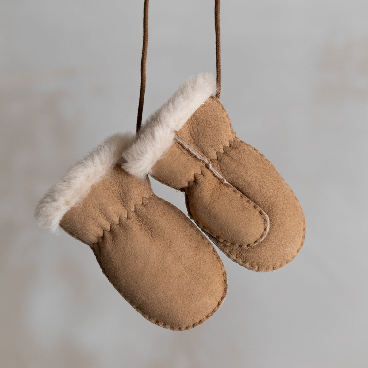 Moufles bébé et enfant en peau d'agneau camel, paire suspendue par son cordon