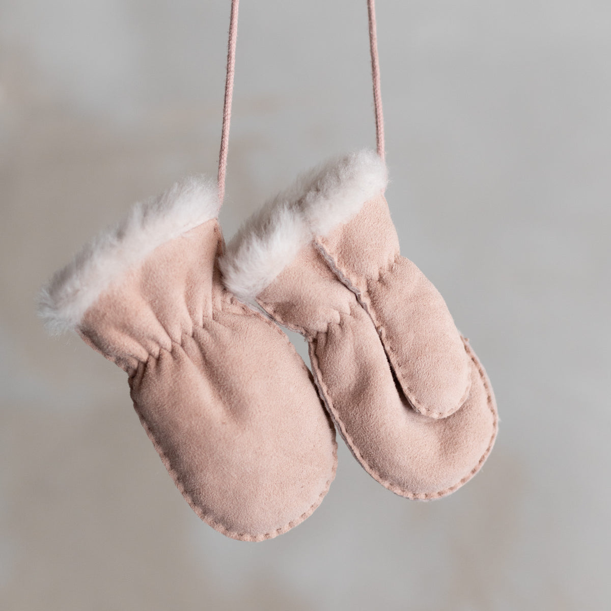 Moufles bébé et enfant en peau d'agneau rose, paire suspendue par son cordon