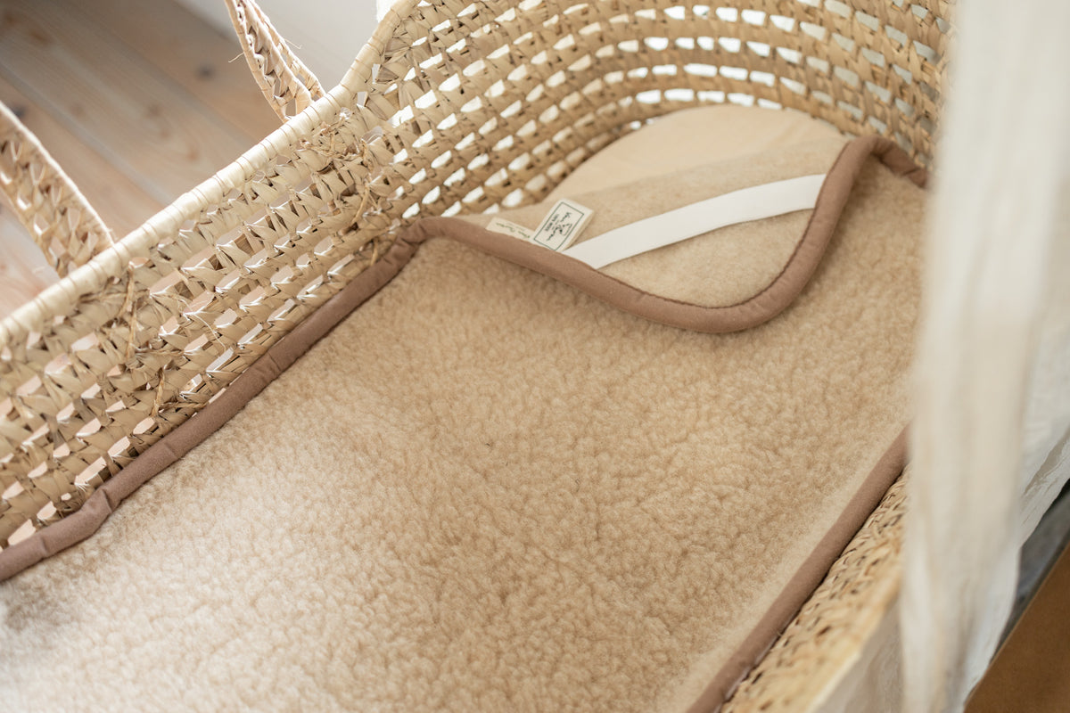 Surmatelas en laine pour berceau et poussette beige, installé dans un couffin en osier